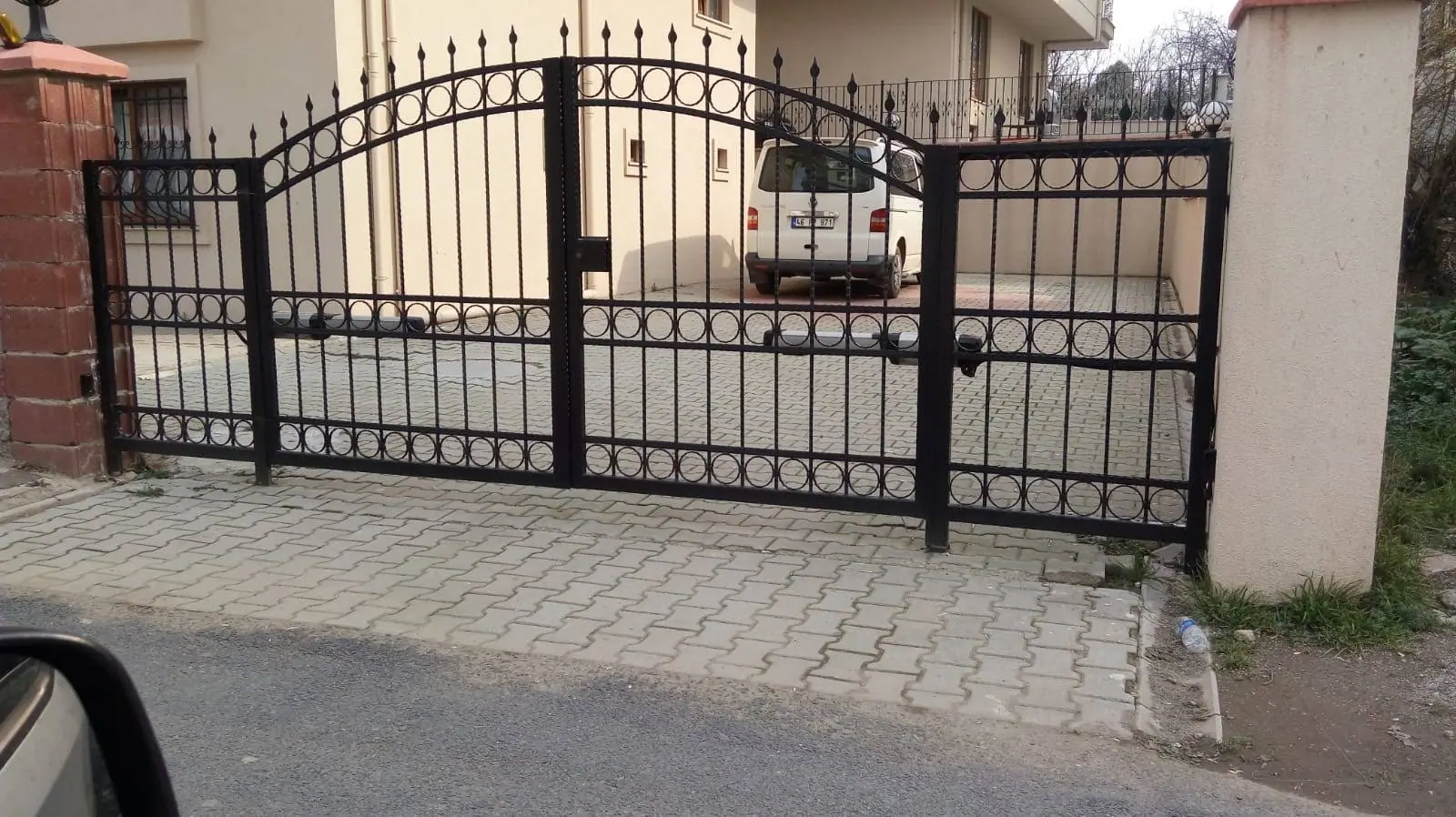 Kilit taşı döşeli giriş önünde kemerli çift kanat ferforje bahçe kapısı