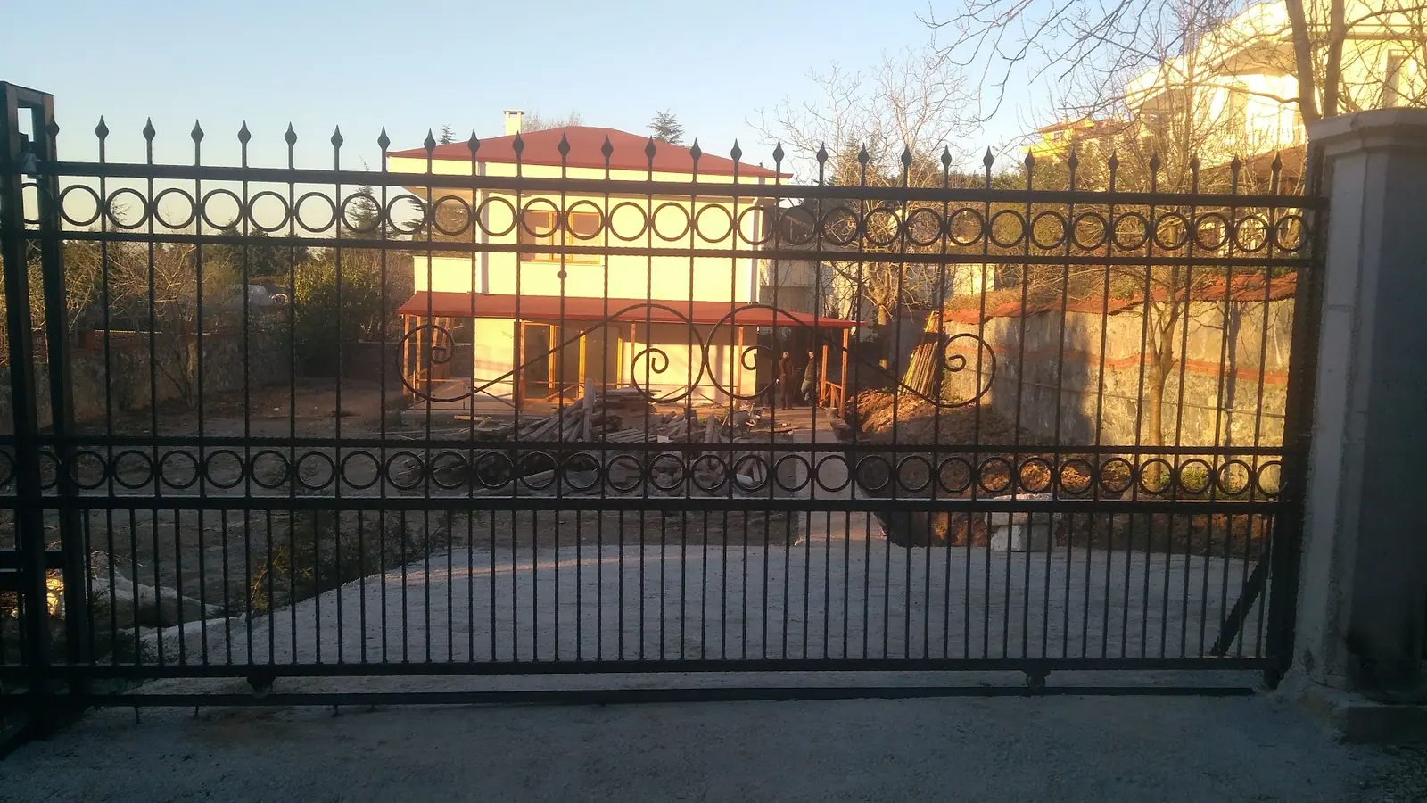 Gün batımında, mızrak uçlu dikmelerle yapılmış uzun bahçe çiti ve kapısı